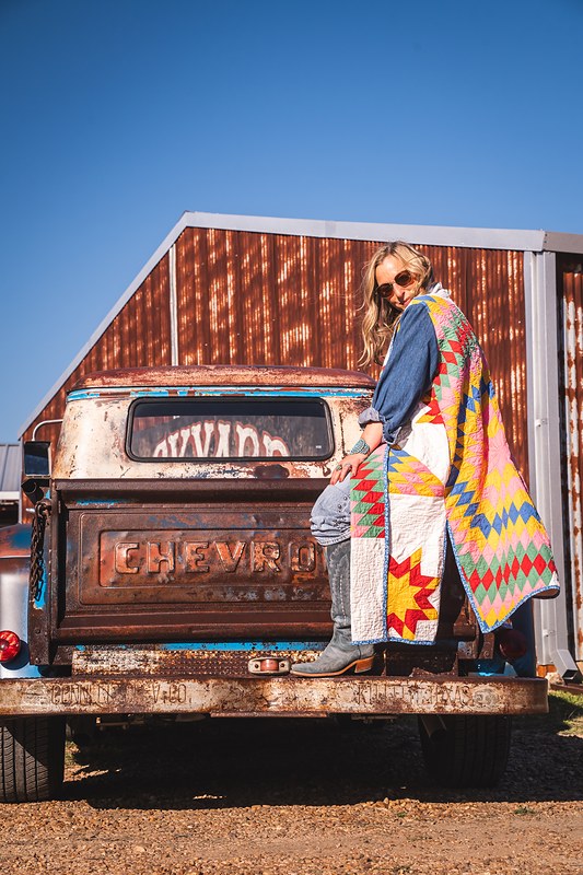 A Lauren Shapiro look seated on a vintage Chevrolet tailgate against a rusted barn, Round Top, Texas